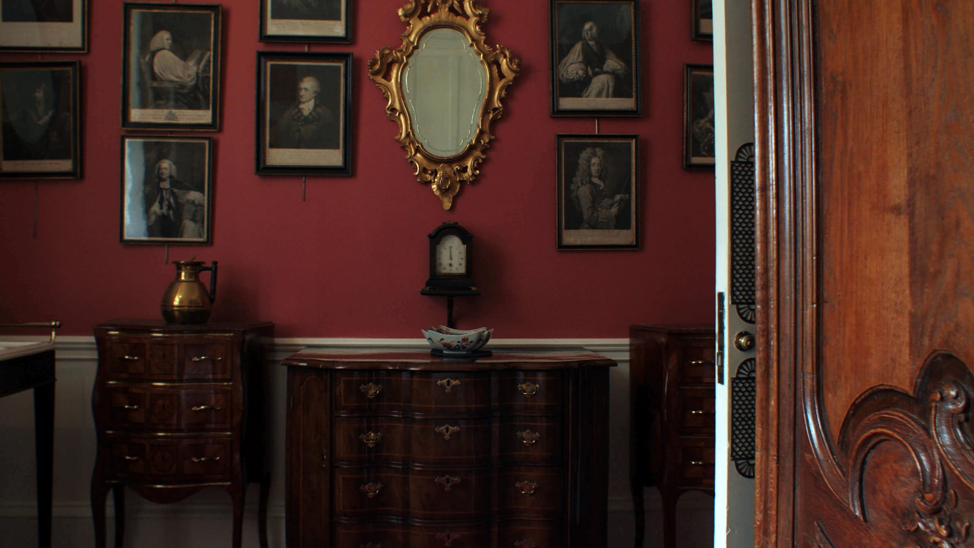 A grand red bathroom filled with portraits and antiques