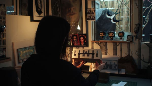 Karen Bones holding a miniature model of a building in a dimly lit room